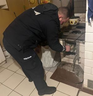 policjant w mieszkaniu mężczyzny przygotowuje piec do rozpalenia ognia