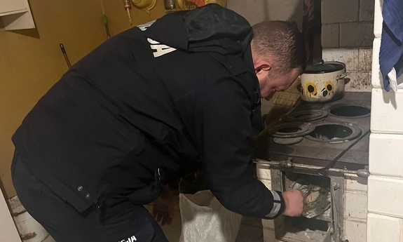 policjant w mieszkaniu mężczyzny przygotowuje piec do rozpalenia ognia