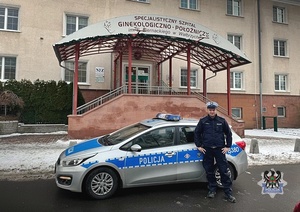 Zdjęcie policjanta przy radiowozie przed budynkiem szpitala