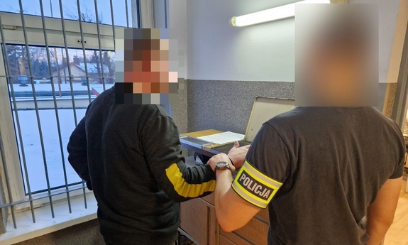 Nieumundurowany policjant stoi z zatrzymanym mężczyzną przy urządzeniu do pobierania odcisków palców