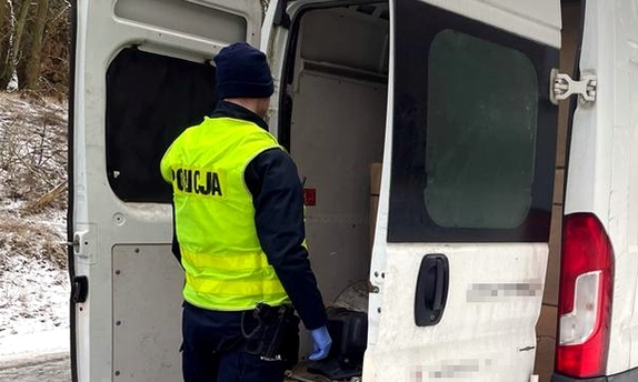 policjant stoi przy busie z otwartymi tylnymi drzwiami, przez które widać kartony