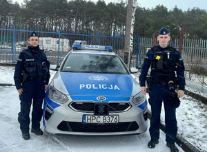 oznakowany radiowóz, obok umundurowani policjantka i policjant