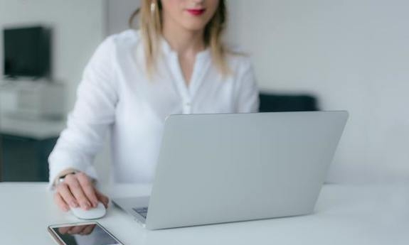 kobieta siedzi przy laptopie, w dłoni trzyma myszkę