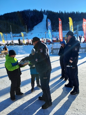 Dwaj policjanci pozują z dorosłym mężczyzną oraz dwójką dzieci, dziewczynka ma na głowie kask narciarski.
