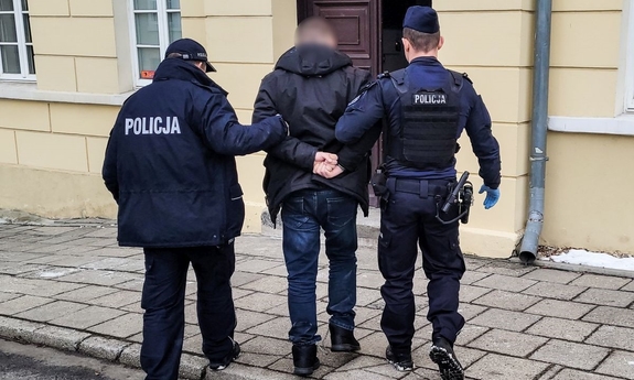 dwóch umundurowanych policjantów prowadzi zatrzymanego mężczyznę