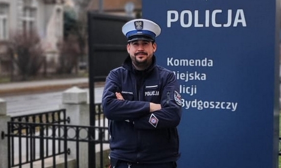 Policjant stoi przy pylonie informacyjnym z napisem Komenda Miejska Policji w Bydgoszczy