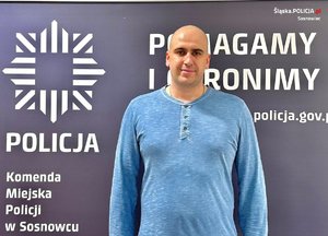 Policjant w cywilnym ubraniu stoi na tle ścianki