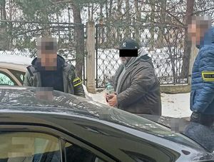 dwóch policjantów prowadzi zatrzymanego mężczyznę do radiowozu