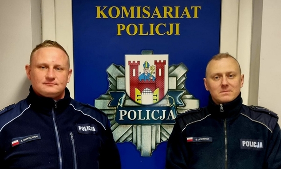 dwóch umundurowanych policjantów stoi na tle baneru Komisariatu Policji