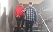 Policjant razem z zatrzymanym mężczyzną wchodzą po schodach. Zatrzymany ma na rękach kajdanki