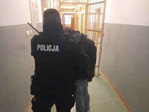 Policjant idzie przez korytarz z zatrzymanym