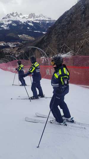 Trójka umundurowanych policjantów stoi na nartach na stoku narciarskim.