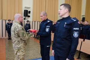 Zastępca Komendanta Głównego Policji nadinsp. Roman Kuster przekazuje złożoną w kostkę flagę Polski policjantowi z JSPP, obok niego stoi Komendant Szkoły Policji w Słupsku