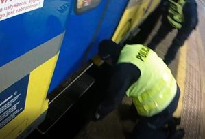 policjant pomaga mężczyźnie, który wpadł między peron, a jadący pojazd szynowy