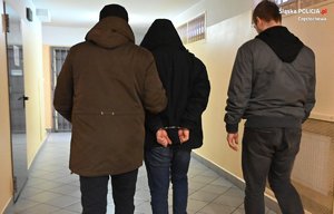 Policjanci prowadzą osobę zatrzymaną korytarzem