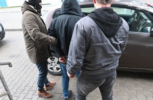 Policjanci prowadzą osobę zatrzymaną. w tle cywilny radiowóz.