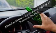 Fragment kierownicy auta widziany z perspektywy kierującego i dłoń z butelką po alkoholu. W poprzek zdjęcia napis: Alkohol za kierownicą może zabrać czyjeś życie! Prowadzę, NIE PIJĘ!