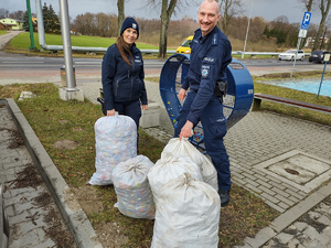 Policjanci stoją przy metalowym sercu na nakrętki. Mają ze sobą białe worki z nakrętkami