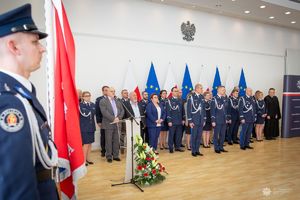 Na pierwszym planie policjant z flagą polski. W tle odznaczeni cywile