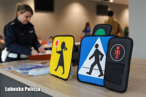 znaki drogowe oraz materiały edukacyjne na stole, obok stoi dziecko i policjant