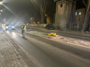 Pora nocna. Policjant ruchu drogowego na jezdni, za nim widoczny samochód. Na pasie rozdzielającym jezdnie widać skoszony żółty słupek, a z tyłu na poboczu uszkodzone auto