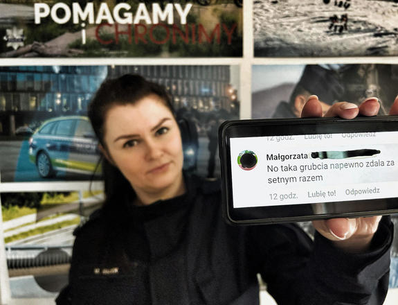 Policjantka trzyma w ręku telefon, na którym wyświetla się obrażający ją wpis jednej z internautek
