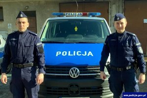 dwóch umundurowanych policjantów stoi przy radiowozie