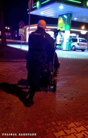 Pora nocna. Widok z tyłu na umundurowanego policjanta, który pcha wózek na stację paliw