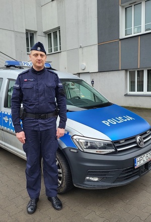 na zdjęciu widać jak umundurowany policjant stoi przy radiowozie