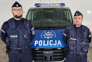 dwóch umundurowanych policjantów stoi przy radiowozie