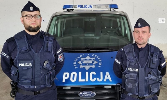 dwóch umundurowanych policjantów stoi przy radiowozie