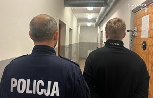 Umundurowany policjant prowadzi korytarzem zatrzymanego. Widok z tyłu