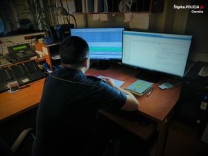 Zdjęcie przedstawia umundurowanego policjanta, który siedzi przed komputerami