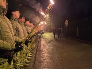 Funkcjonariusze w szeregu z płonącymi pochodniami w dłoniach, przed nimi przechodzi minister swia i  zastępca komendanta głównego Policji