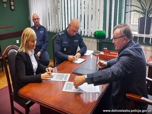 osoby podpisujące akt notarialny siedzą za biurkiem i podpisują dokumenty