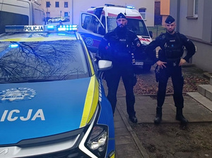 dwaj policjanci stoją obok radiowozu