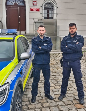 dwaj umundurowani policjanci przy radiowozie