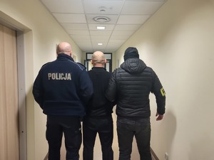 policjanci prowadzą zatrzymanego przez korytarz