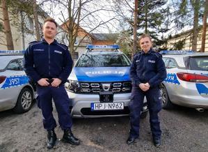 policjant i policjantka stoją przed radiowozem policyjnym