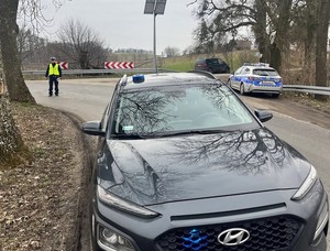 Zabezpieczone narkotykifunkcjonariusz na drodze, przy drodze zaparkowane radiowozy i inne samochody