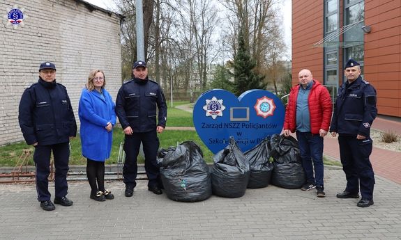 umundurowani policjanci i dwie osoby cywilne stoją przy sercu Zarząd NSZZ Policjantów w Szkole Policji w Pile, przed nimi stoją worki z zakrętkami