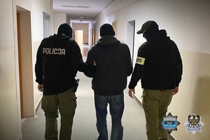 Policjanci prowadzą zatrzymanego przez korytarz