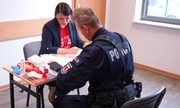 policjant siedzi przy stoliku naprzeciwko kobiety wypełniając formularz