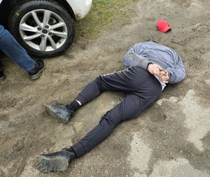 Na zdjęciu zatrzymany mężczyzna w kajdankach leży na ziemi. W tle noga mężczyzny i koło pojazdu