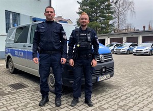 dwóch umundurowanych policjantów stoi przy radiowozie