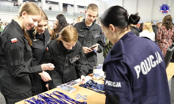 policjantka przy stoisku promocyjnym i uczniowie klasy policyjnej oglądający gadżety promocyjne