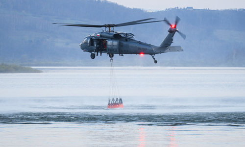 Policyjny śmigłowiec z podwieszonym zbiornikiem na wodę.