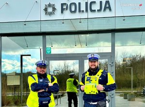 Zdjęcie przedstawia dwóch umundurowanych policjantów z wydziału ruchu drogowego na tle komendy w Sosnowcu