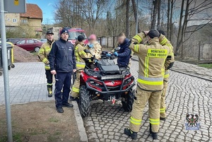 policjanci i strażacy stojący przy quadzie z uratowaną starszą kobietą