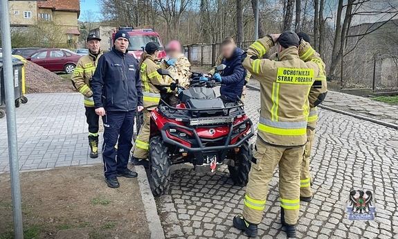 policjanci i strażacy stojący przy quadzie z uratowaną starszą kobietą